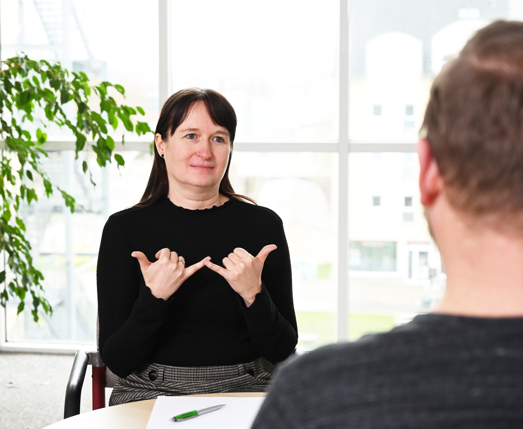 Es sind ein Mann und eine Frau in einer Beratungssituation zu sehen. Die Frau zeigt mit den Händen eine Gebärde.